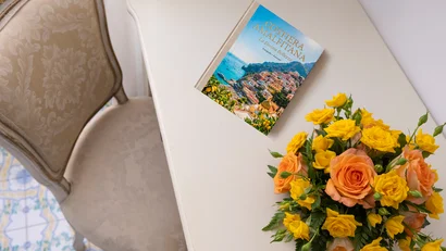Libro sulla Costiera Amalfitana e bouquet di rose gialle e arancioni su scrivania bianca