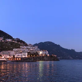 Costa illuminata di un villaggio sul mare al crepuscolo con montagne sullo sfondo