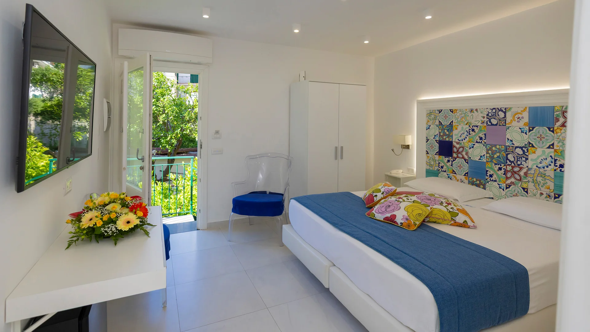 Bright hotel room with double bed and open door to green balcony