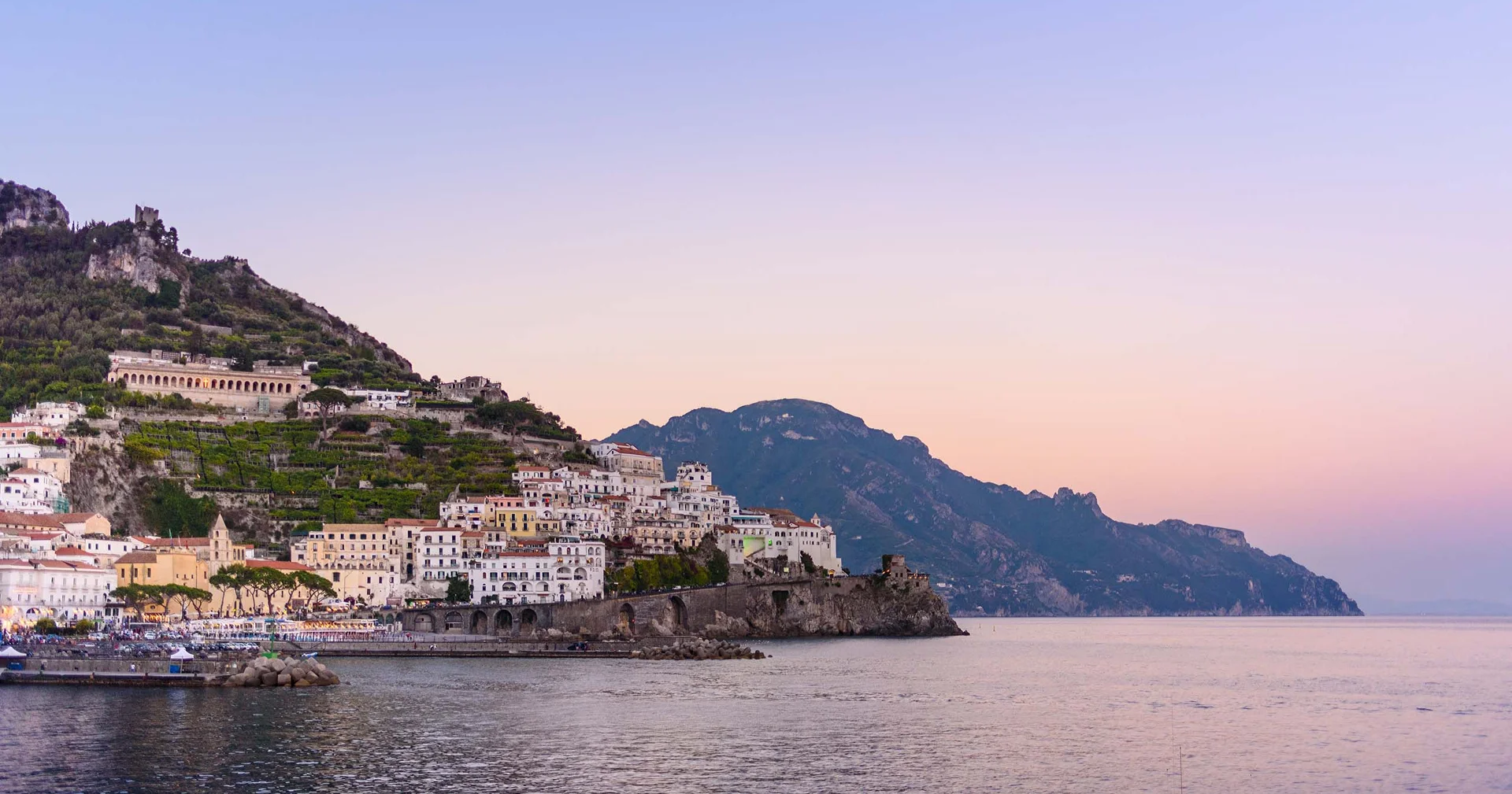 Hotel Amalfi. 3 stelle di design che brillano sulla Costiera Amalfitana. Veduta del villaggio costiero con case bianche su una collina al tramonto